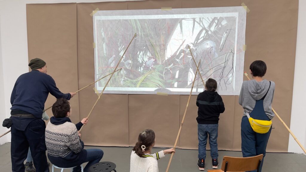 vier Kinder und ein Erzieher malen mit Stöckern ein auf eine Leinwand projiziertes Papgeienbild nach.