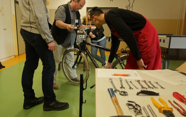 Jemand zeigt, wie man einen Lenker eines Fahrrads justiert und drei weitere Personen schauen zu