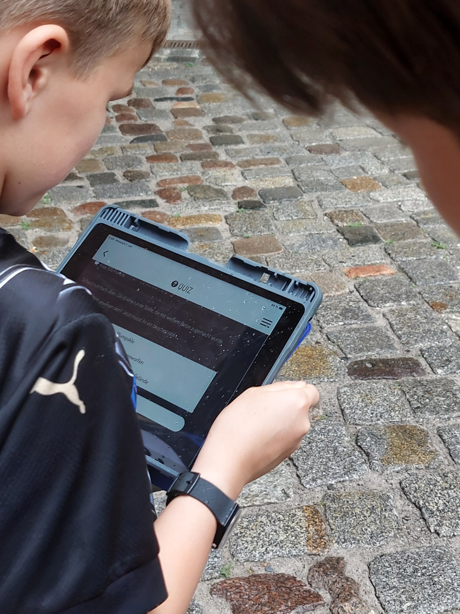 Kinderköpfe schauen auf ein Tablet während sie auf Straßenpflaster stehen